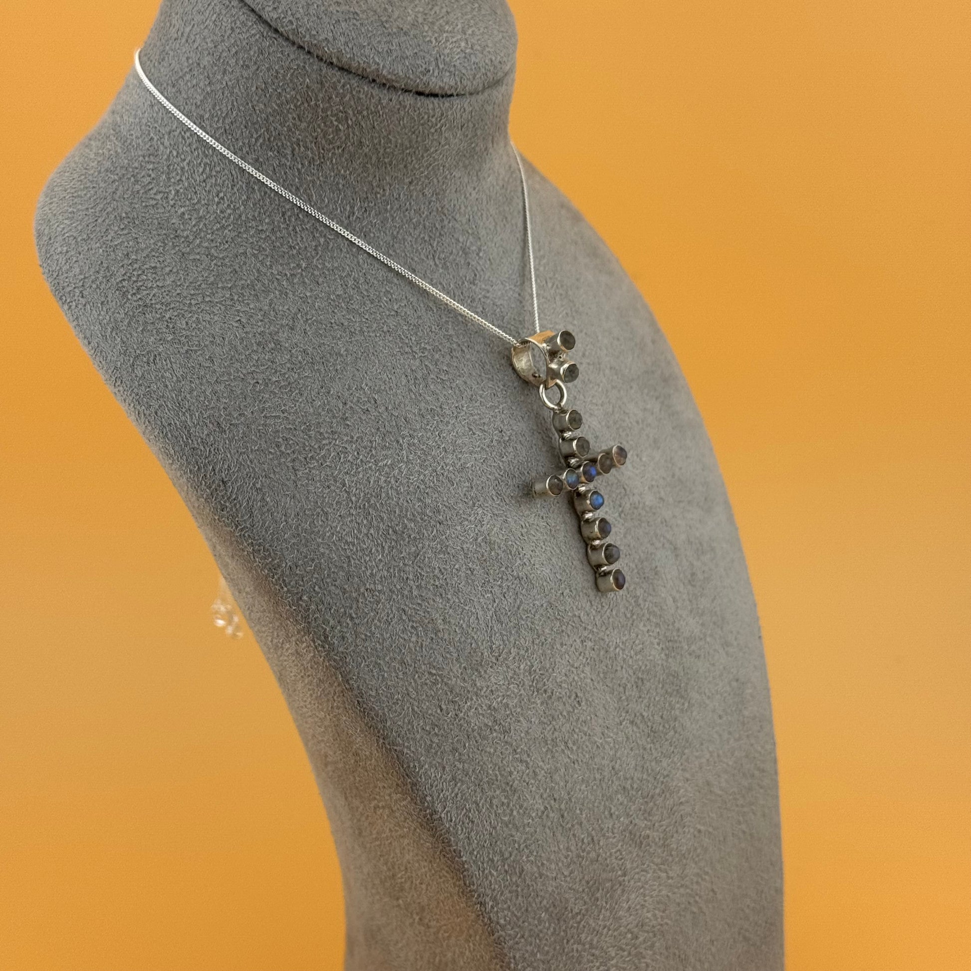 Necklace with a cross pendant on a gray mannequin bust against an orange background