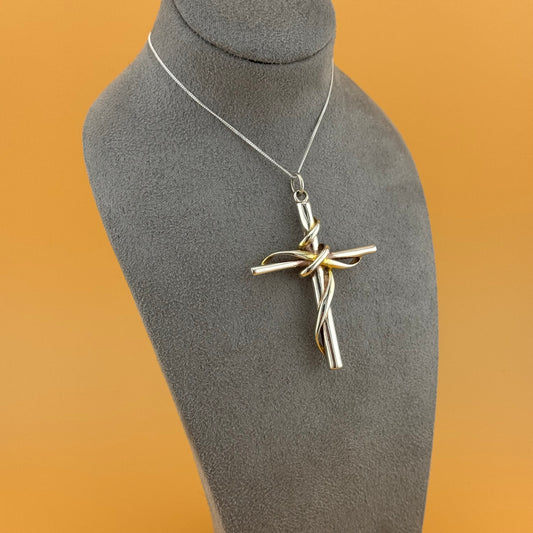 Silver cross pendant on a gray mannequin bust with a brown background