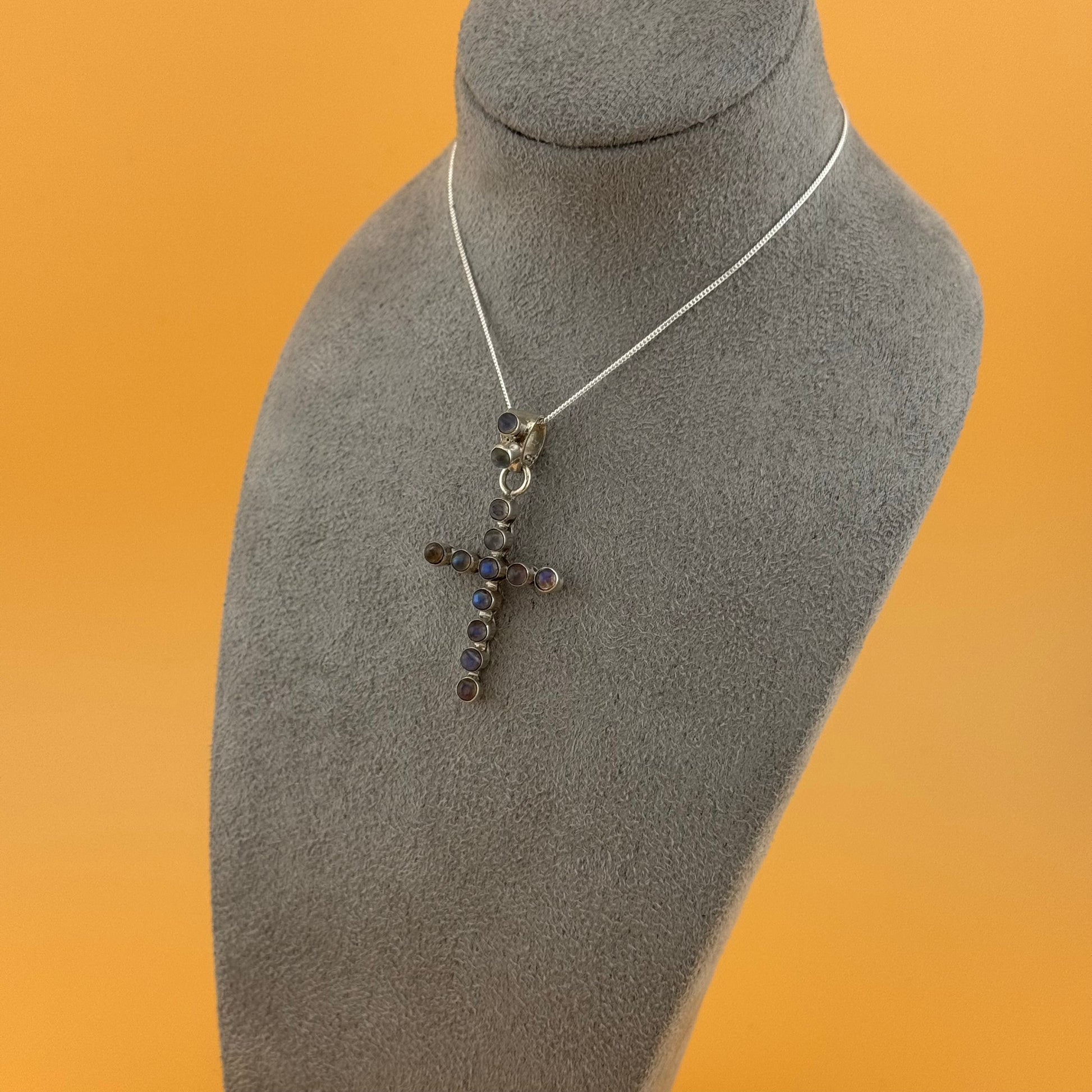 Necklace with a cross pendant on a mannequin bust against an orange background