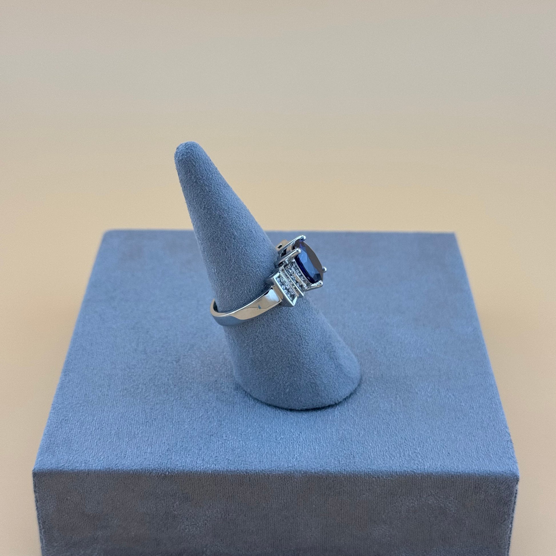 Silver ring with a deep blue sapphire gemstone on a blue stand against a beige background