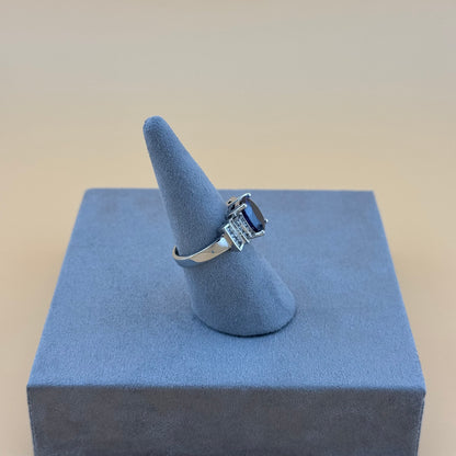 Silver ring with a deep blue sapphire gemstone on a blue stand against a beige background