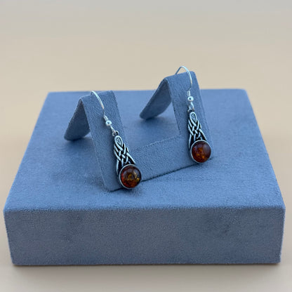 Pair of silver amber earrings with amber stones on a blue jewelry display box.