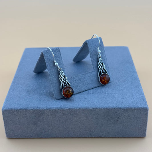 Pair of silver amber earrings with amber stones on a blue jewelry display box.