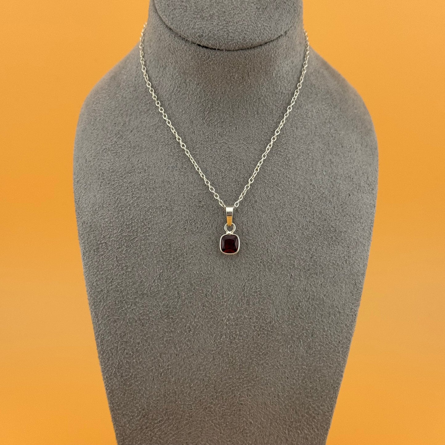 Necklace with garnet pendant on a gray mannequin bust against an orange background