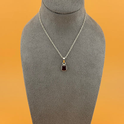 Necklace with garnet pendant on a gray mannequin bust against an orange background
