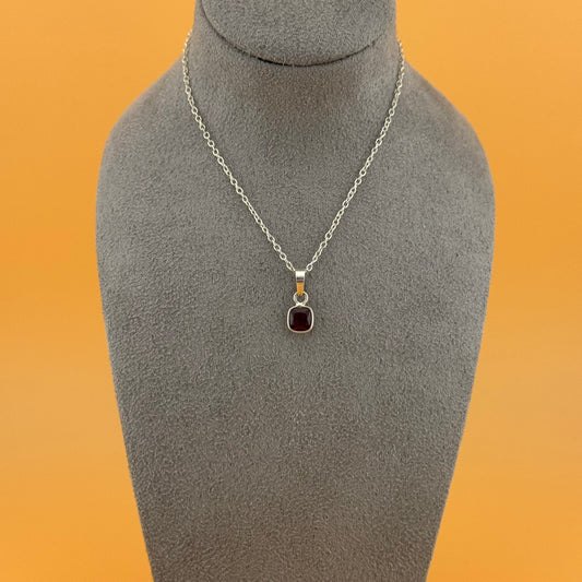 Necklace with garnet pendant on a gray mannequin bust against an orange background