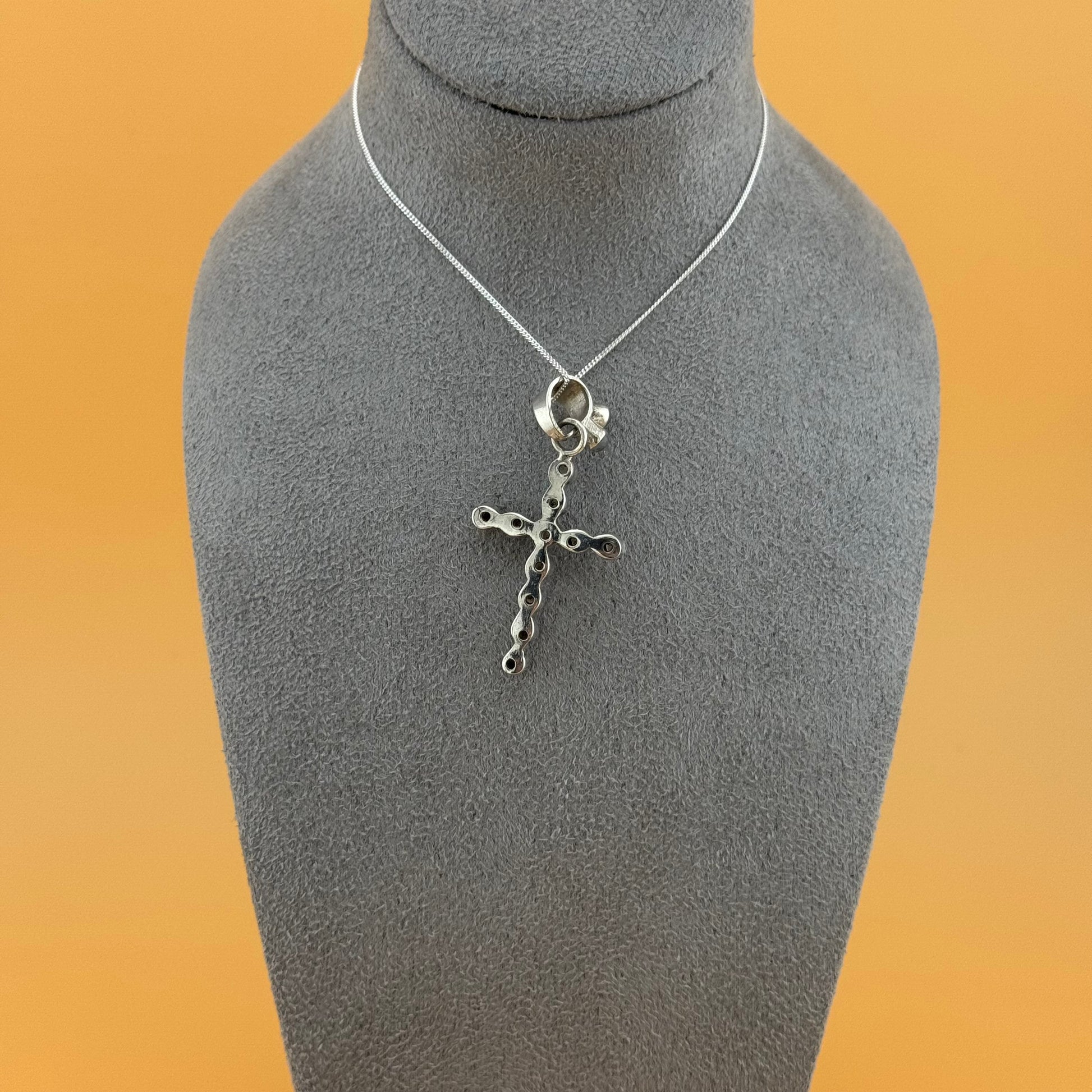 Silver cross necklace on a gray mannequin bust against an orange background