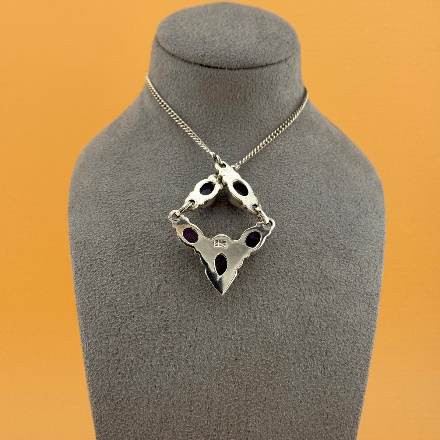 Silver necklace with a unique pendant on a gray bust against an orange background