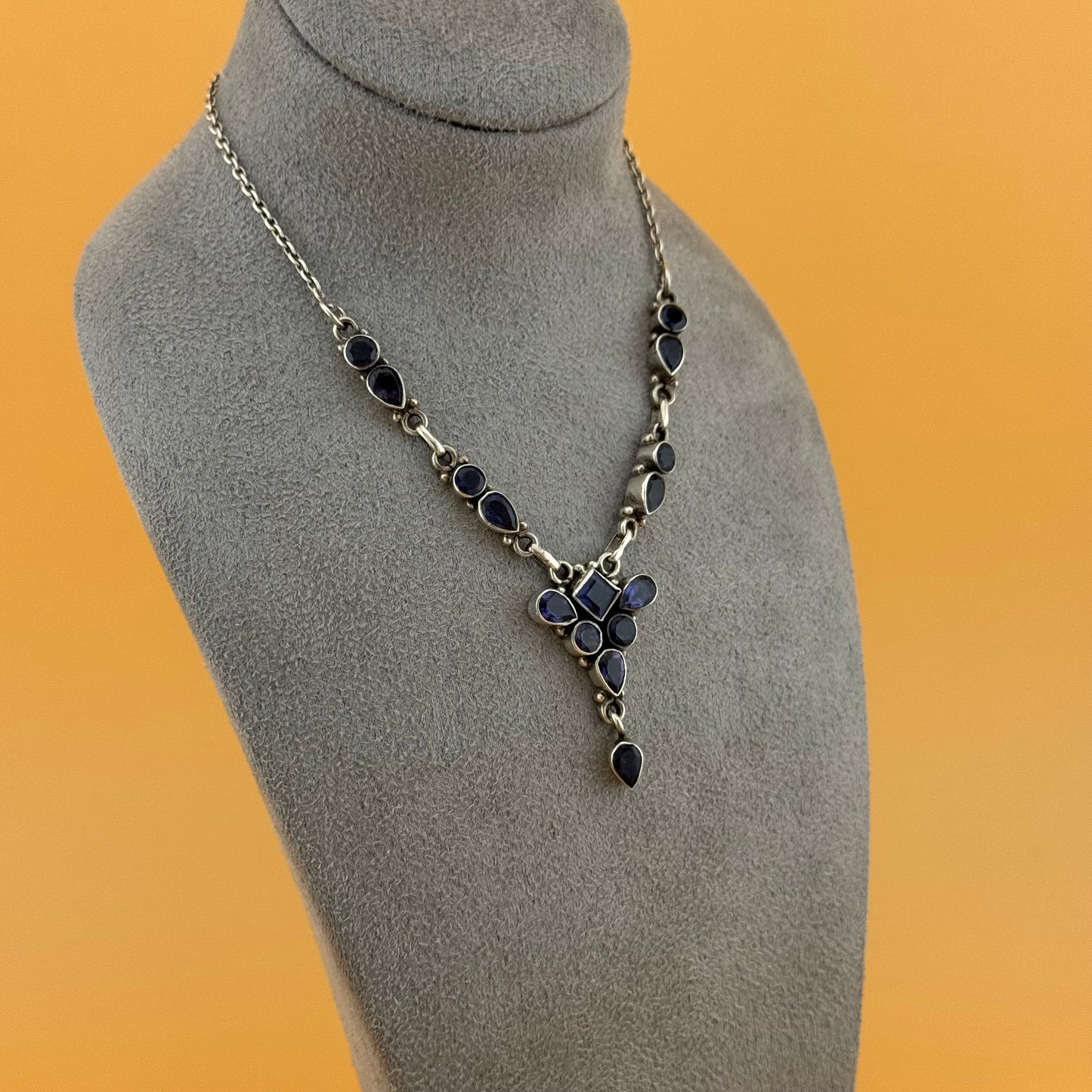 Necklace with blue iolite stones on a gray mannequin bust against an orange background