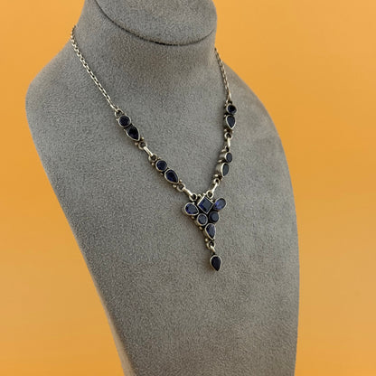 Necklace with blue iolite stones on a gray mannequin bust against an orange background