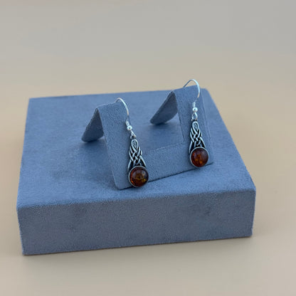 Pair of silver amber earrings with amber stones on a blue jewelry display box.