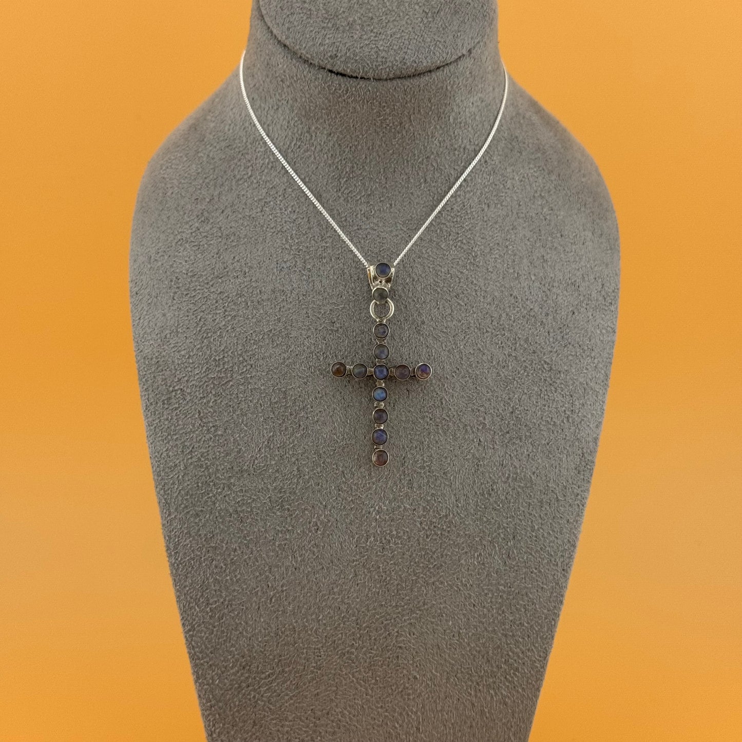 Necklace with a labradorite cross pendant on a mannequin bust against an orange background