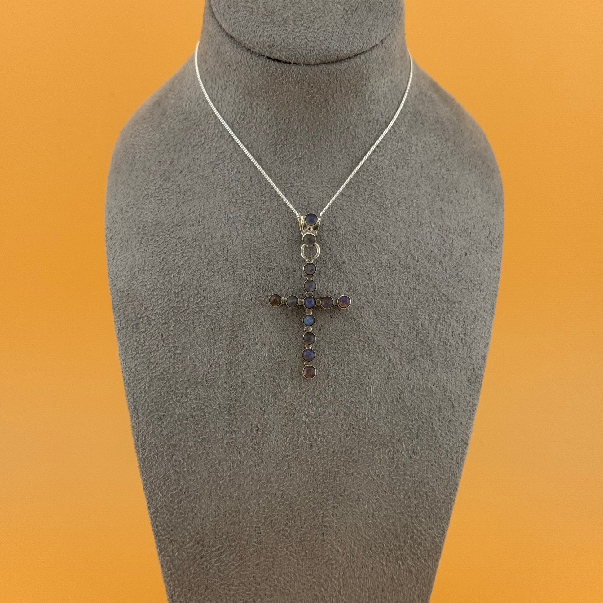 Necklace with a labradorite cross pendant on a mannequin bust against an orange background