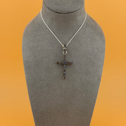 Necklace with a labradorite cross pendant on a mannequin bust against an orange background