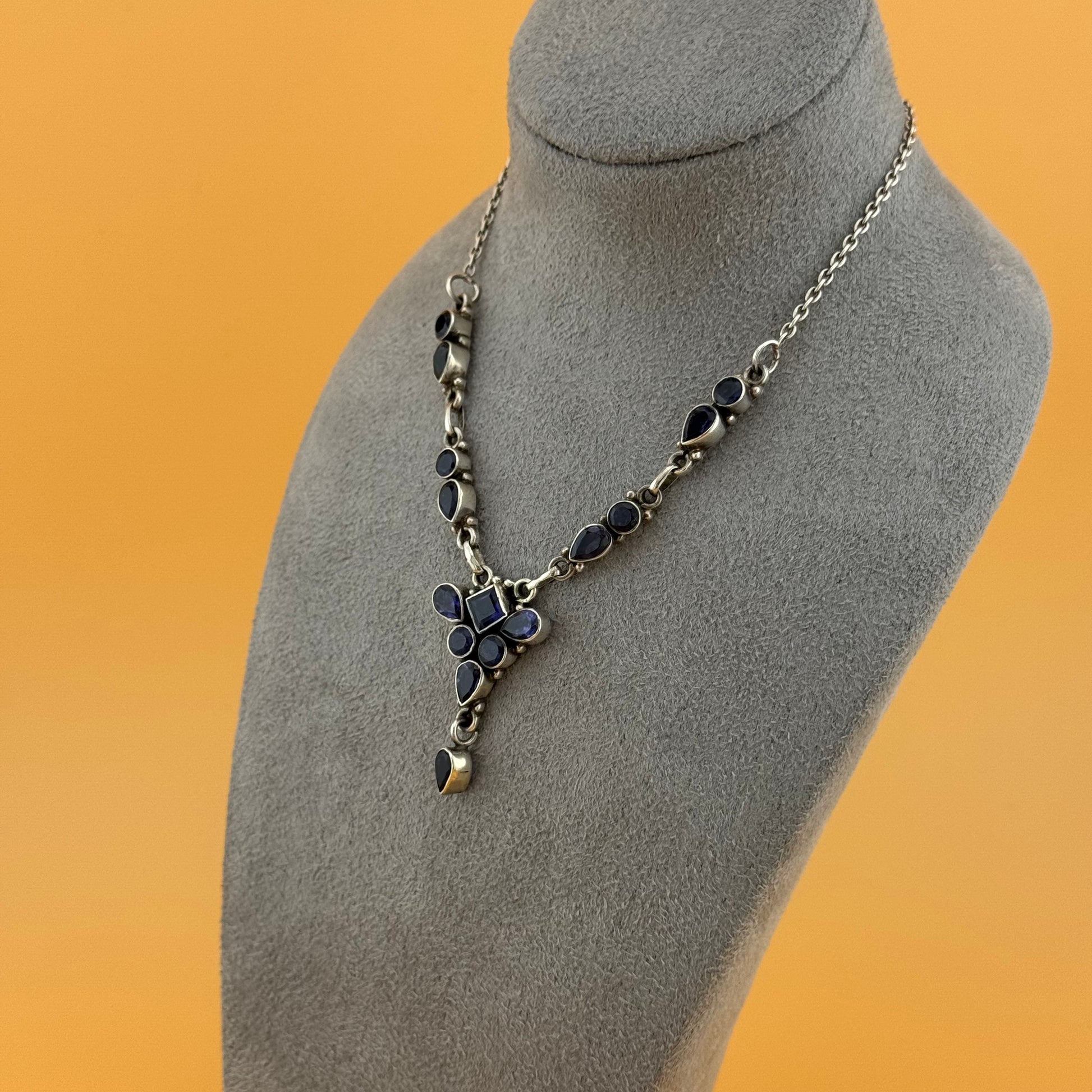 Necklace with blue floral pendants on a gray mannequin bust against an orange background