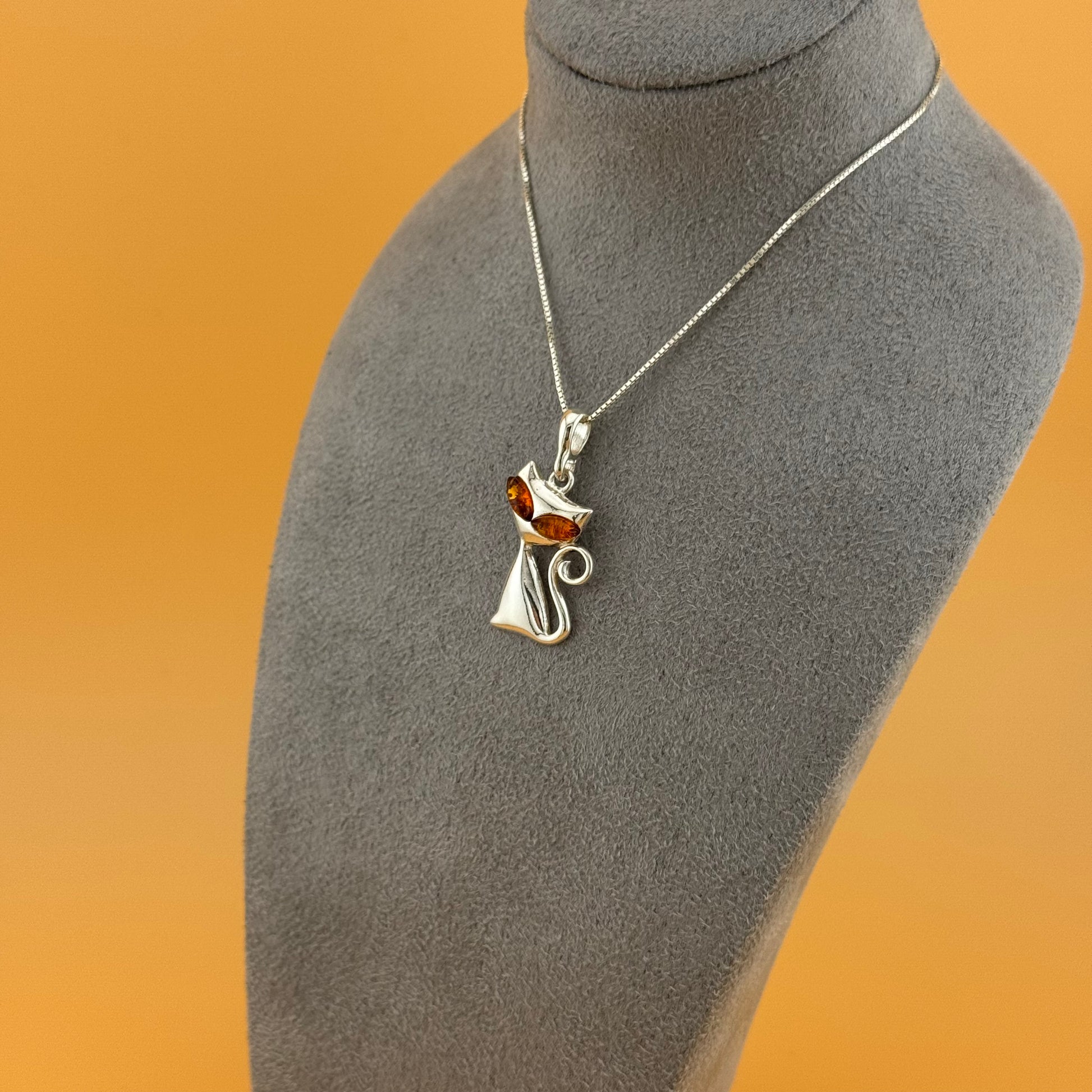 Silver necklace with a cat-shaped pendant on a gray mannequin bust against an orange background