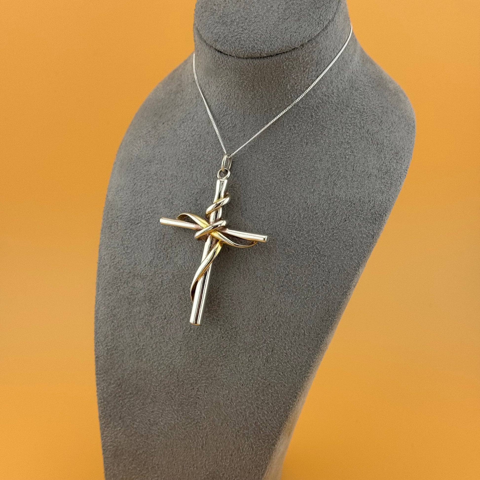 Silver cross pendant on a gray mannequin bust with an orange background