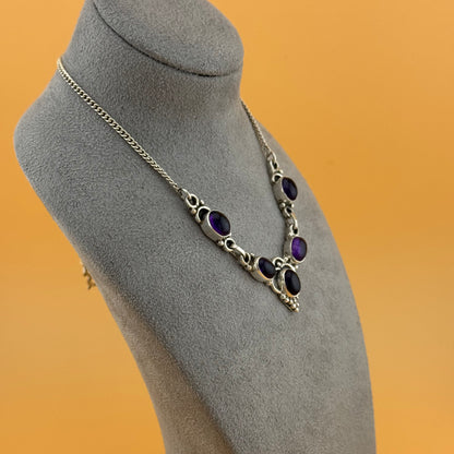 Necklace with purple stones on a gray mannequin bust against an orange background