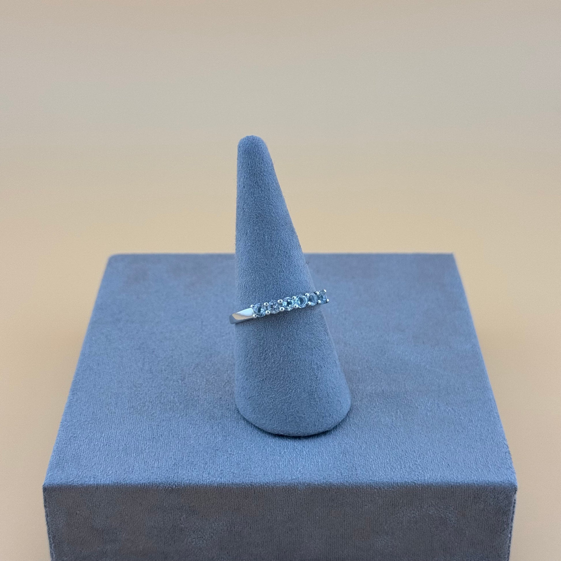 Silver ring on a blue cone-shaped stand against a beige background