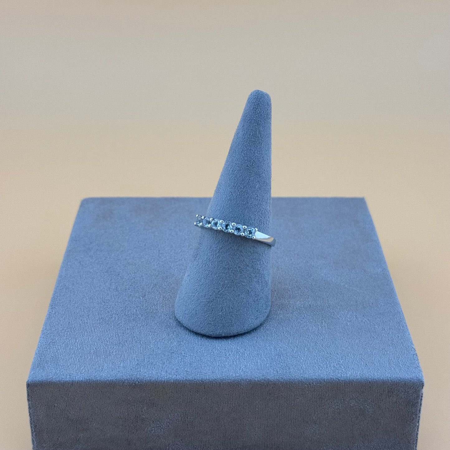 Silver ring on a blue cone-shaped stand against a beige background