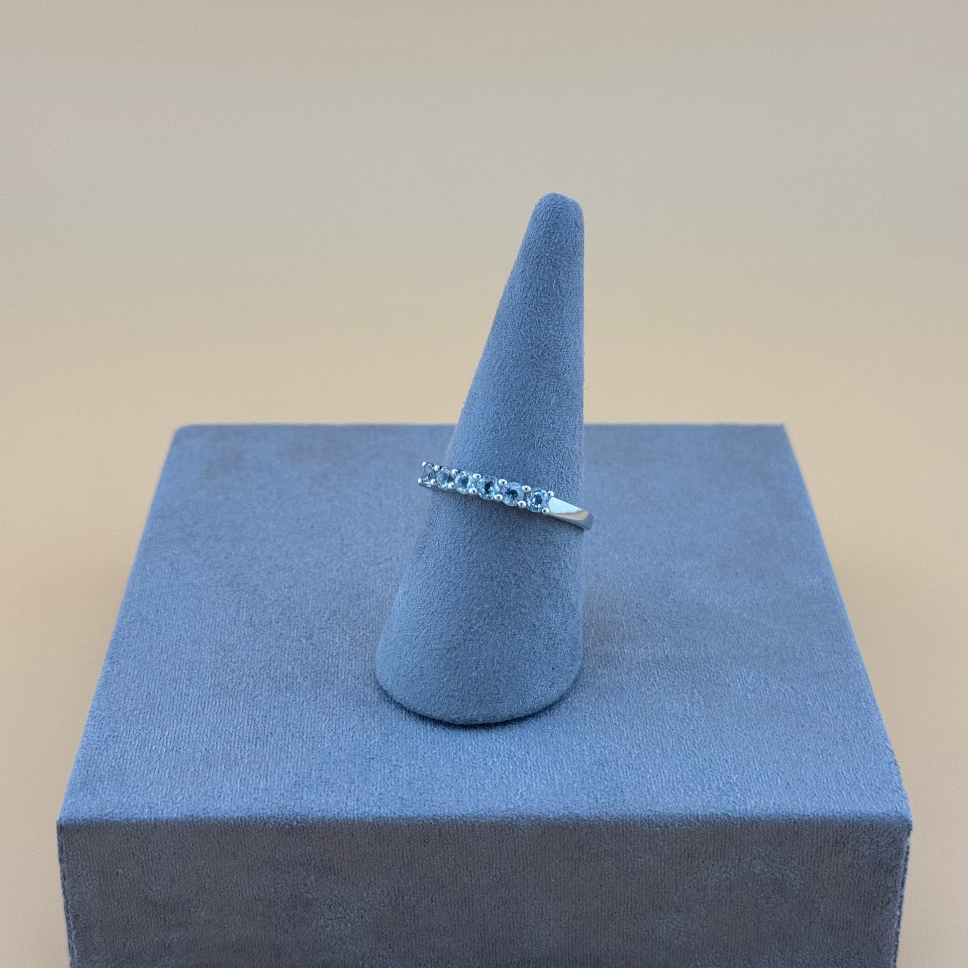 Silver ring on a blue cone-shaped stand against a beige background