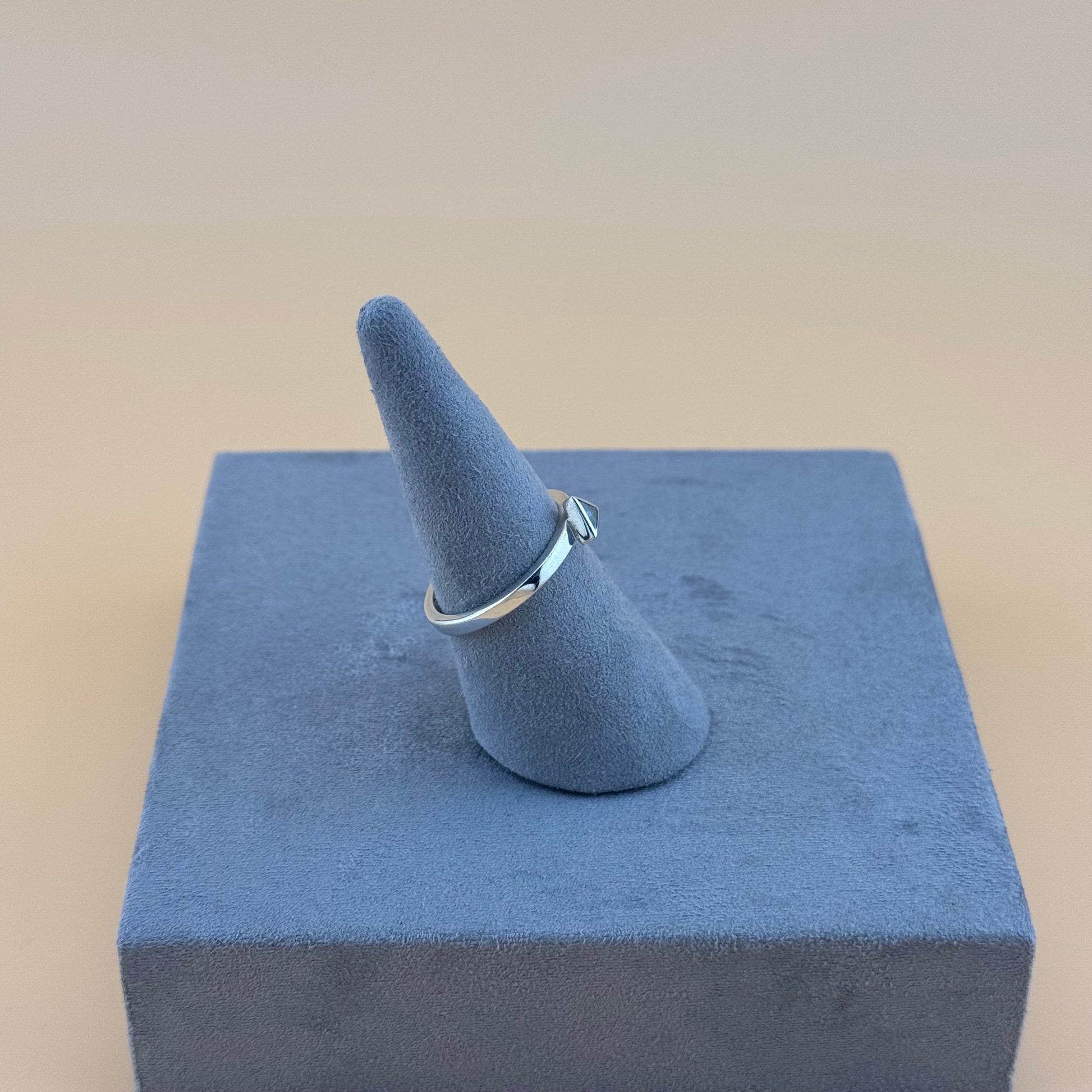 Silver ring on a blue cone-shaped jewelry stand against a beige background