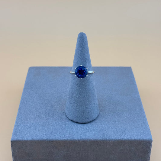 Ring with a blue gemstone on a blue stand against a beige background