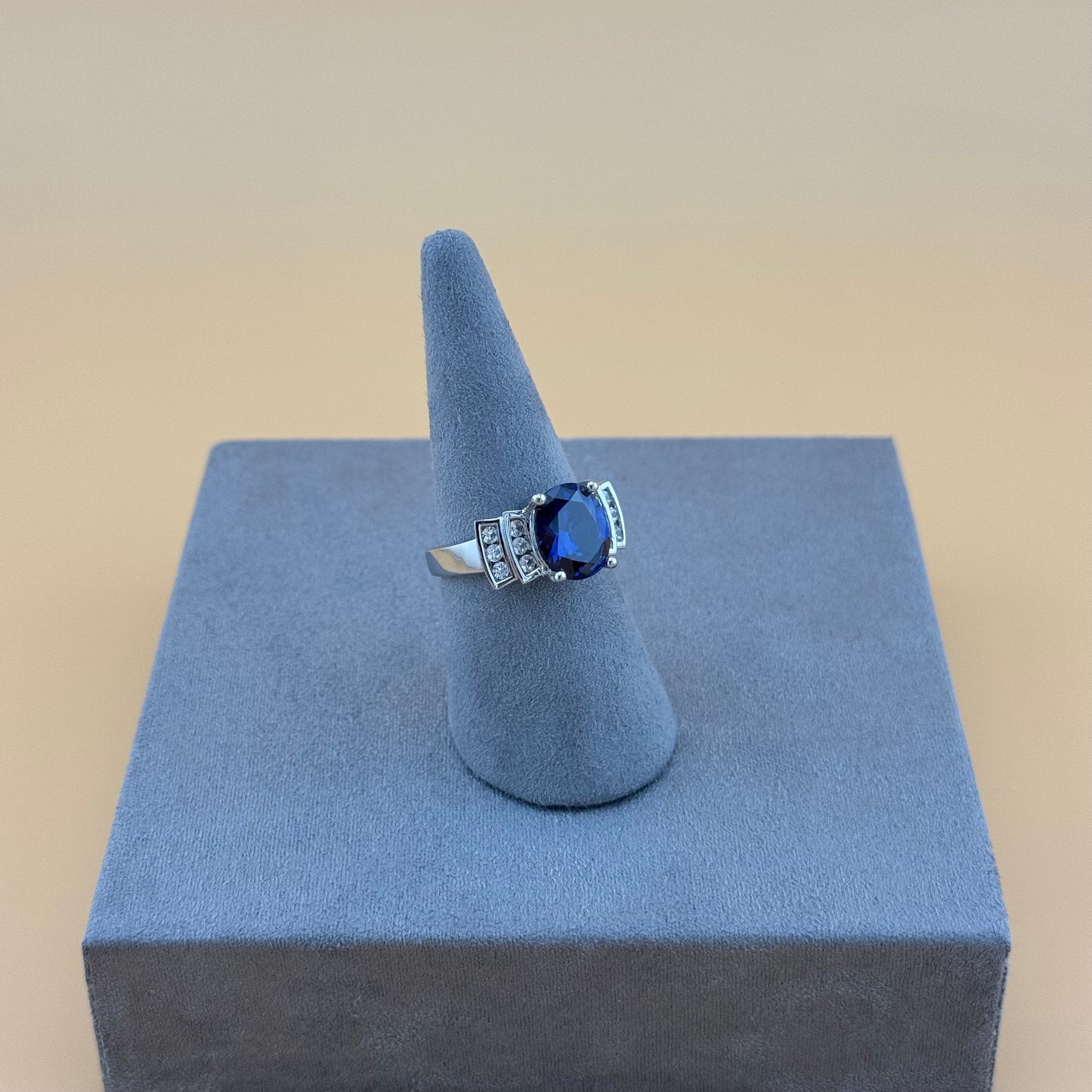 Ring with a blue sapphire gemstone on a gray stand against a beige background