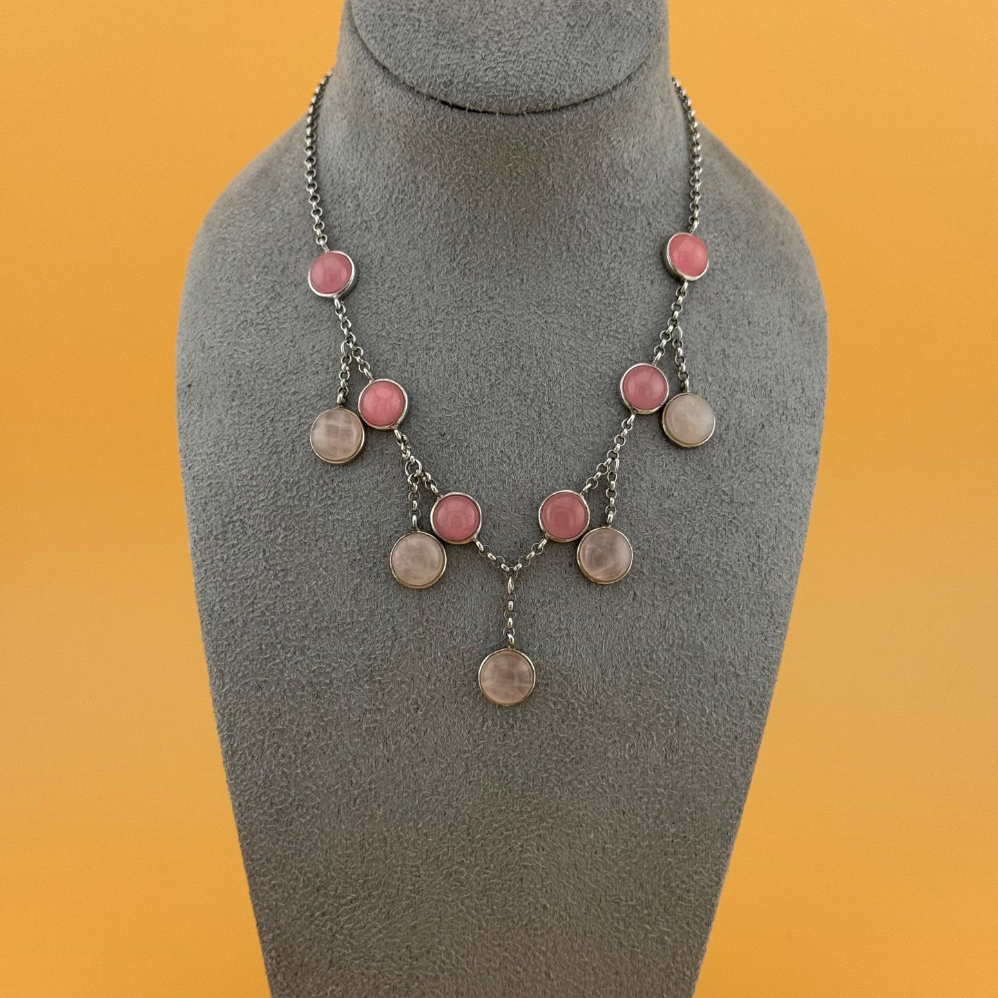 Necklace with rose quartz pink and silver circular pendants on a gray bust against an orange background