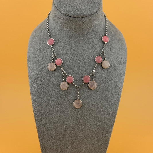 Necklace with rose quartz pink and silver circular pendants on a gray bust against an orange background