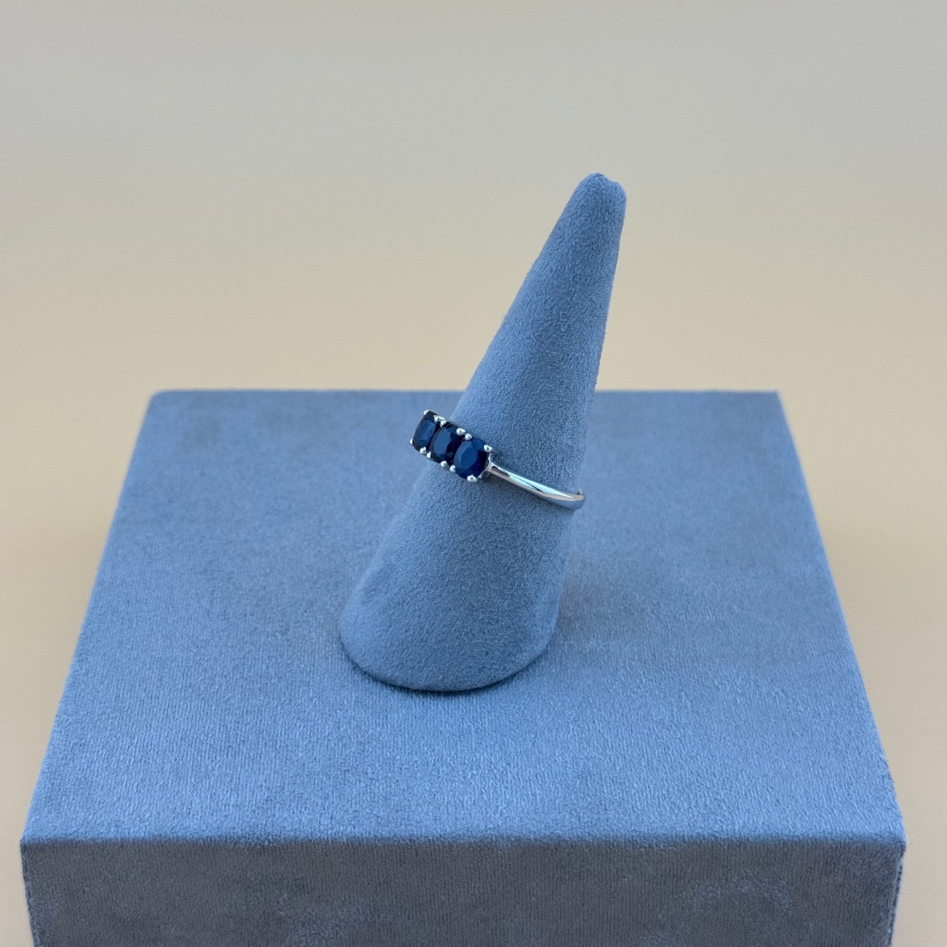 Silver ring with blue sapphire stones on a blue cushioned stand against a beige background