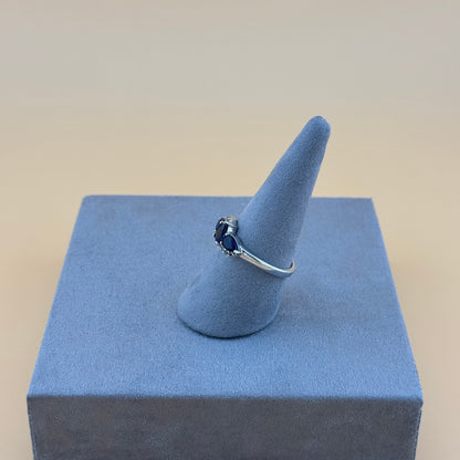 Silver ring with a blue tanzanite gemstone on a blue cone-shaped stand against a beige background