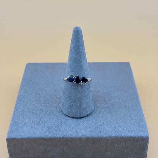 Silver tanzanite ring with a blue gemstone on a blue stand against a beige background