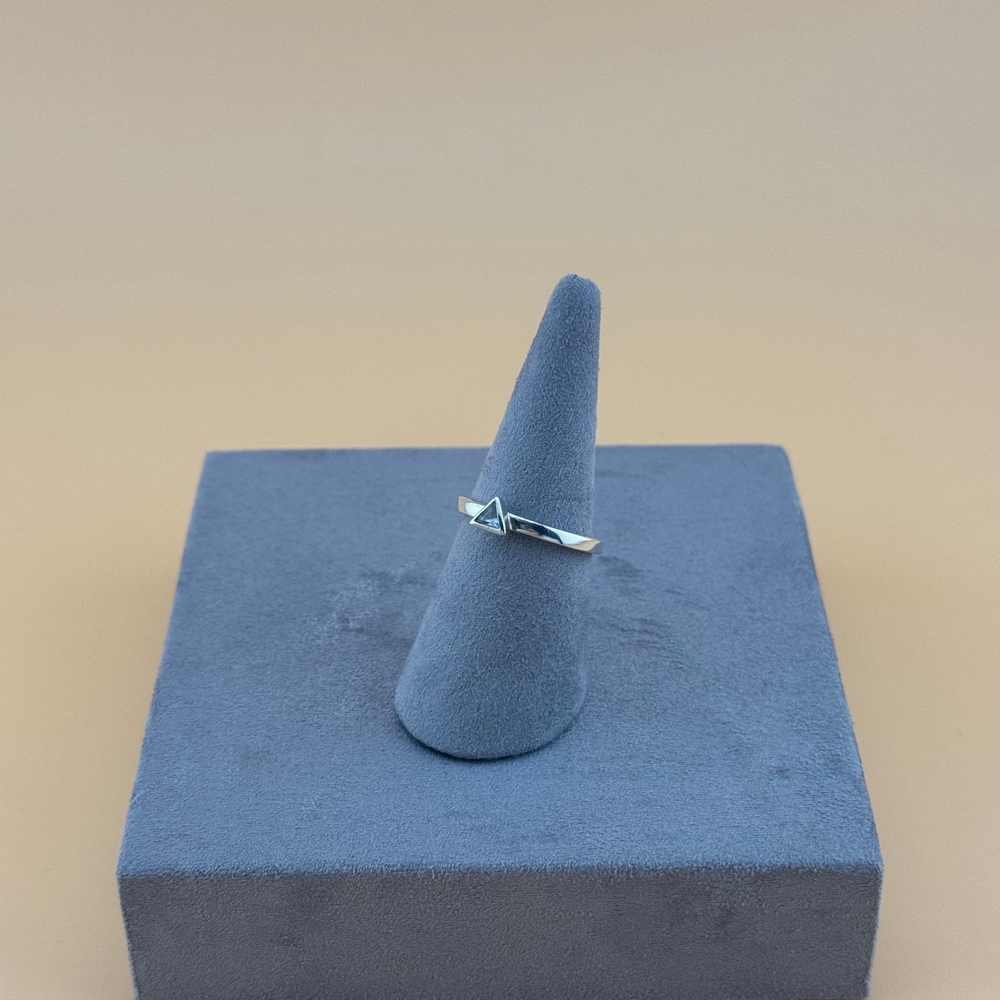 Silver ring on a blue cone-shaped stand against a beige background