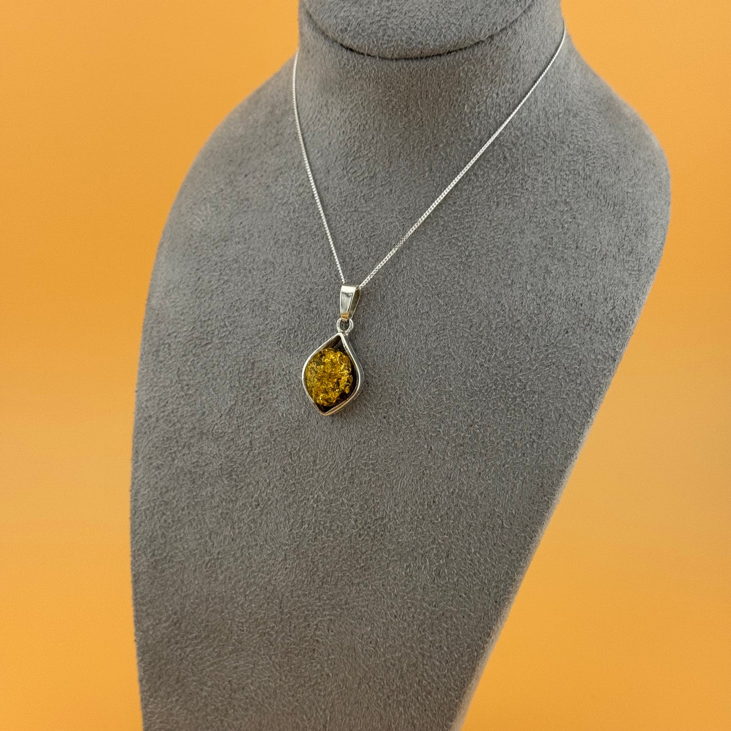 Teardrop-shaped pendant with a yellow amber stone on a mannequin bust against an orange background